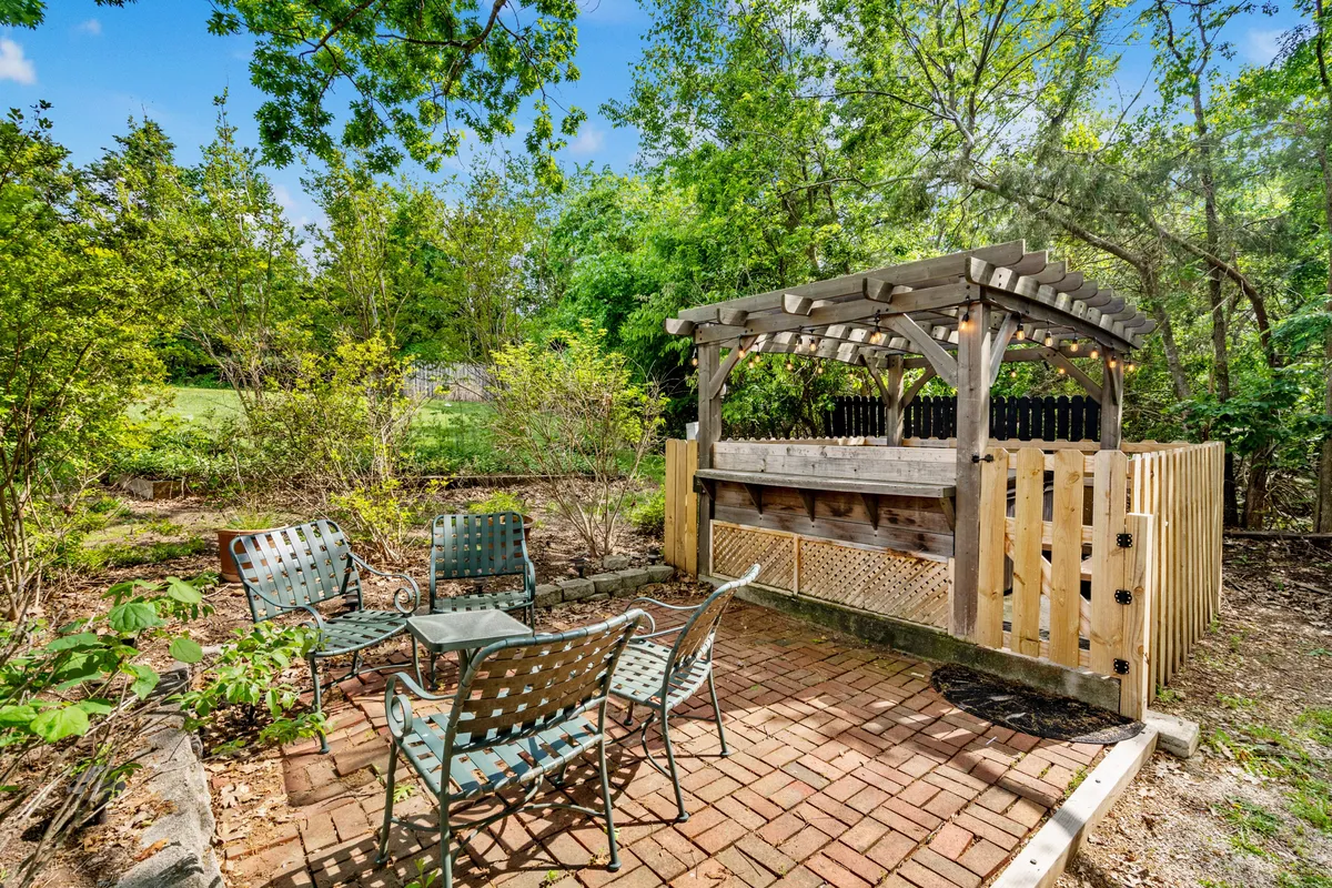 A brick patio with an outdoor bar and a comfortable seating area, surrounded by greenery. The space is clearly designed for group gatherings, outdoor dining, and relaxed social interactions, capturing the energy of picnics, grilling, and festive lakeside barbecues.