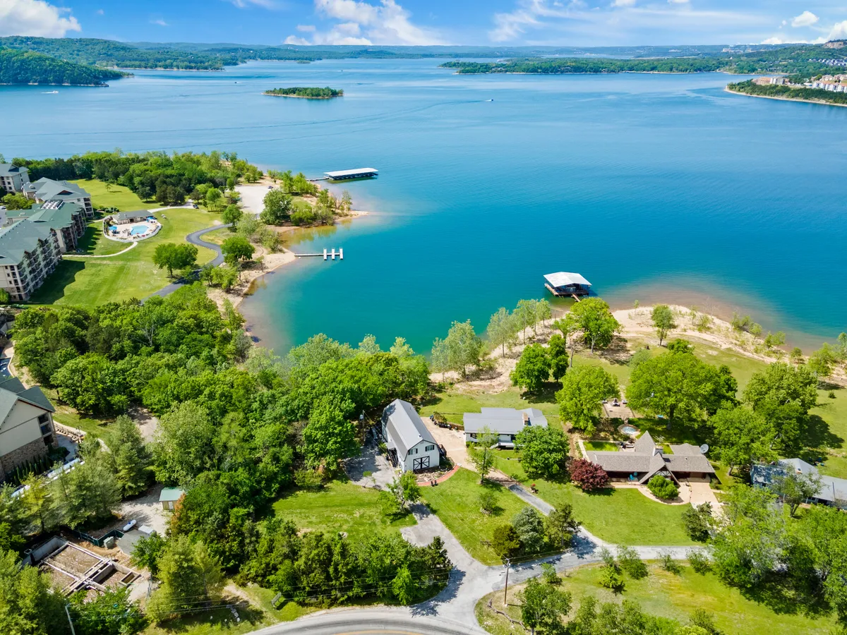 A wide shot of a peaceful lake bordered by lush greenery, featuring a dock that extends out over the water. Residential properties are visible in the background, and the scene exudes a tranquil atmosphere perfect for boating, fishing, swimming, picnicking, and hiking.
