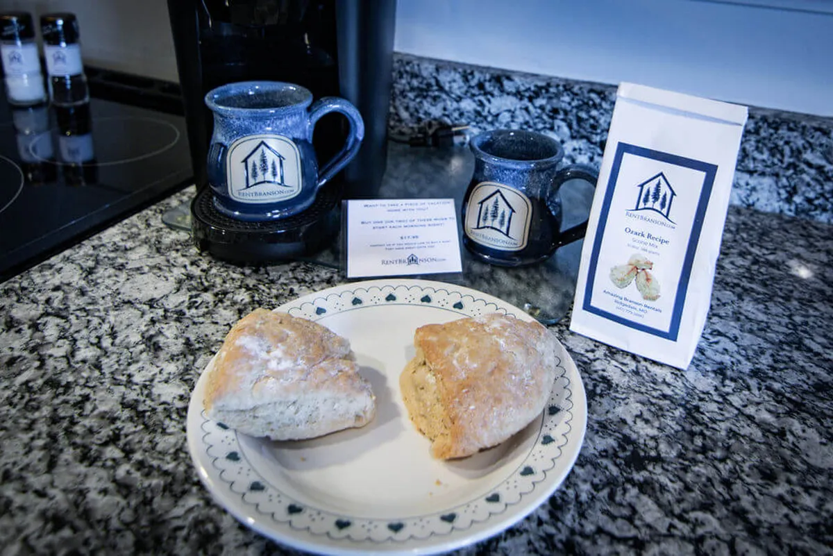 A close-up of a coffee maker with mugs, scones, and a coffee packet on a cozy kitchen countertop. The scene exudes warmth and hospitality, emphasizing morning routines and the joy of sharing coffee and treats.