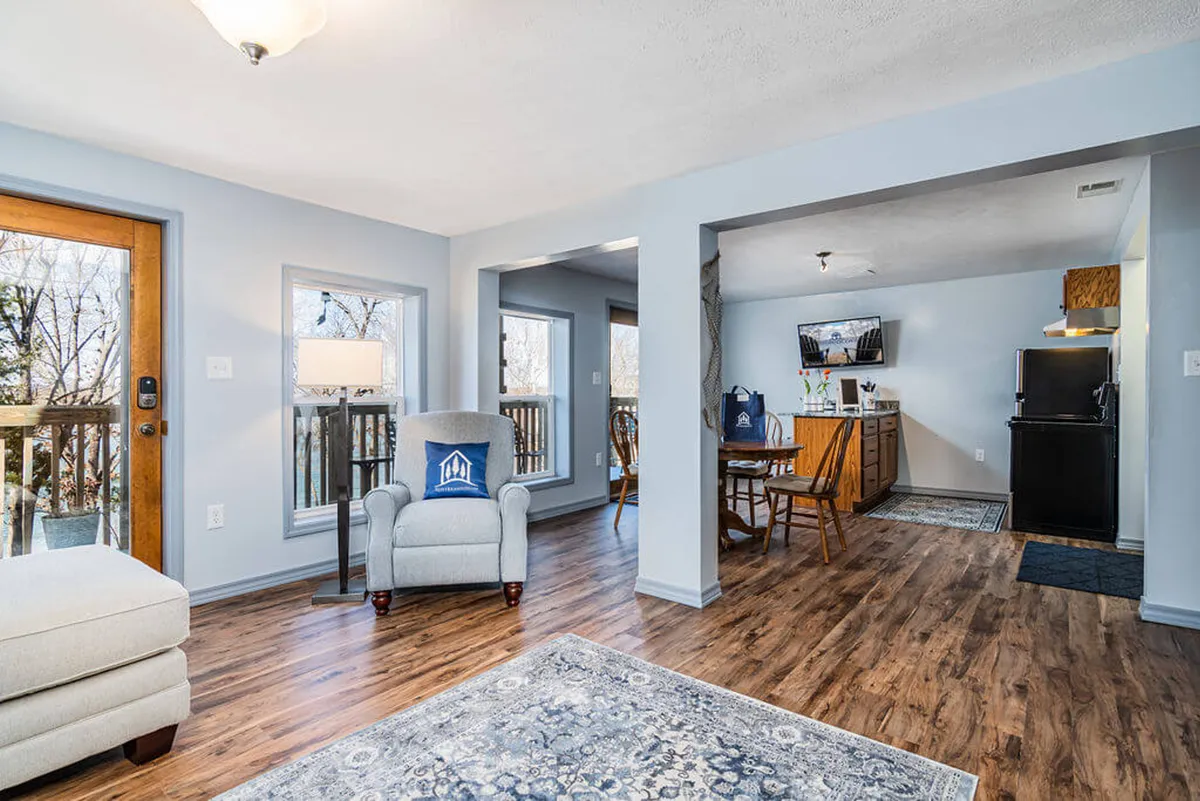 An inviting dining area is visible, with a comfortable armchair, large windows flooding the space with natural light, and a welcoming dining table. The setup hints at relaxed family meals, game nights, and bright mornings with coffee.