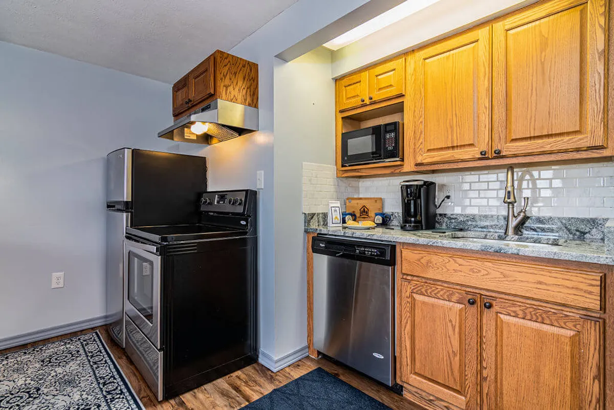 A cozy view of the kitchen featuring black appliances, wooden cabinets, and a granite countertop. The scene feels inviting and practical, with ample space for baking sessions and group meal preparation.