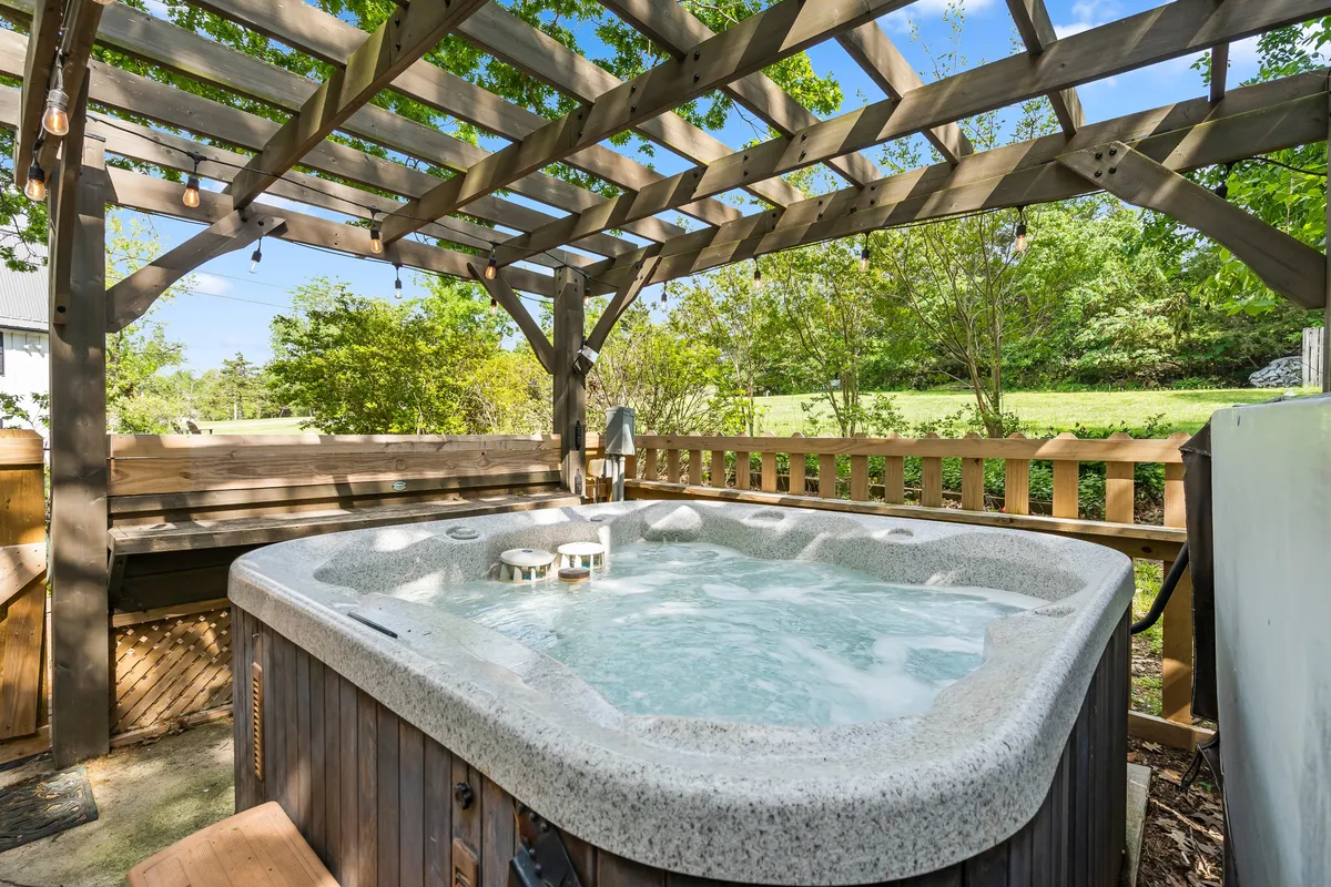 The image features a spacious outdoor hot tub beneath a wooden pergola, surrounded by lush greenery. The setting feels private yet communal, inviting guests to relax while still being part of the vibrant lakeside scene described. The area is clean and well-maintained, with ample space for groups or families to gather.