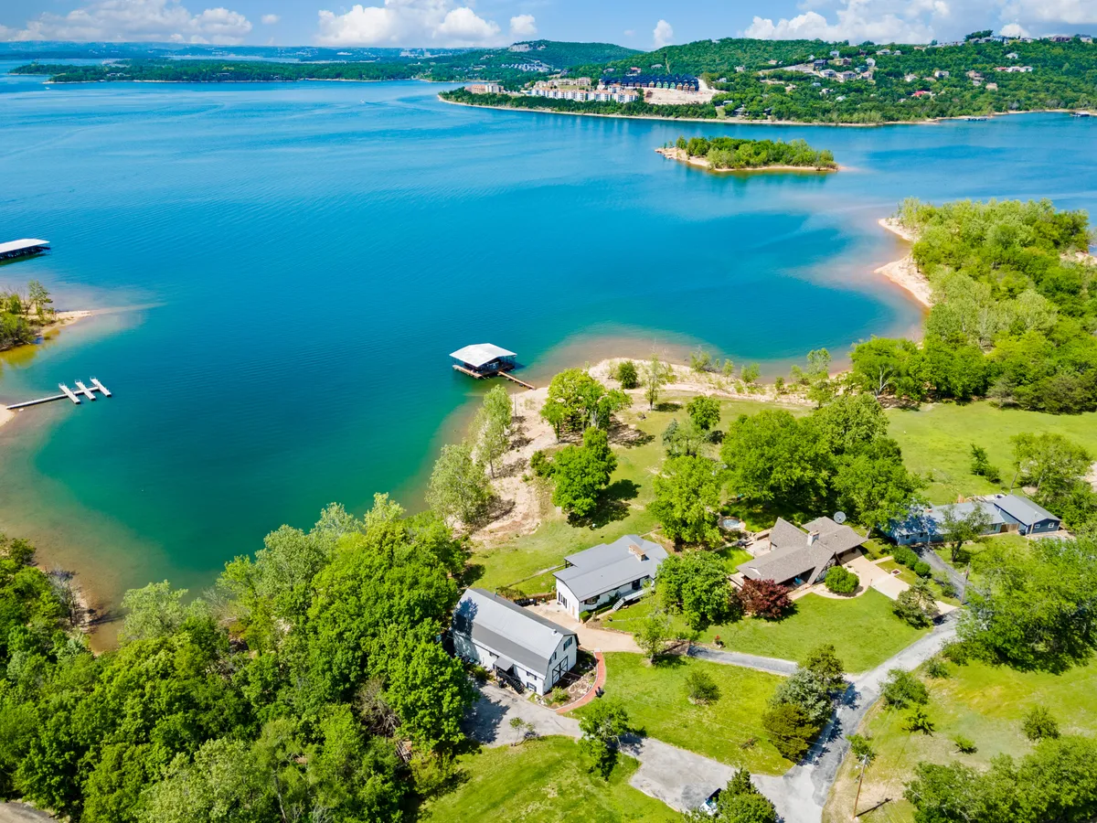 A tranquil lake bordered by abundant greenery and several residential properties. A dock juts out into the water, inviting boating, fishing, or peaceful contemplation. The scene is set for group gatherings, with space for outdoor activities and sunset viewing.